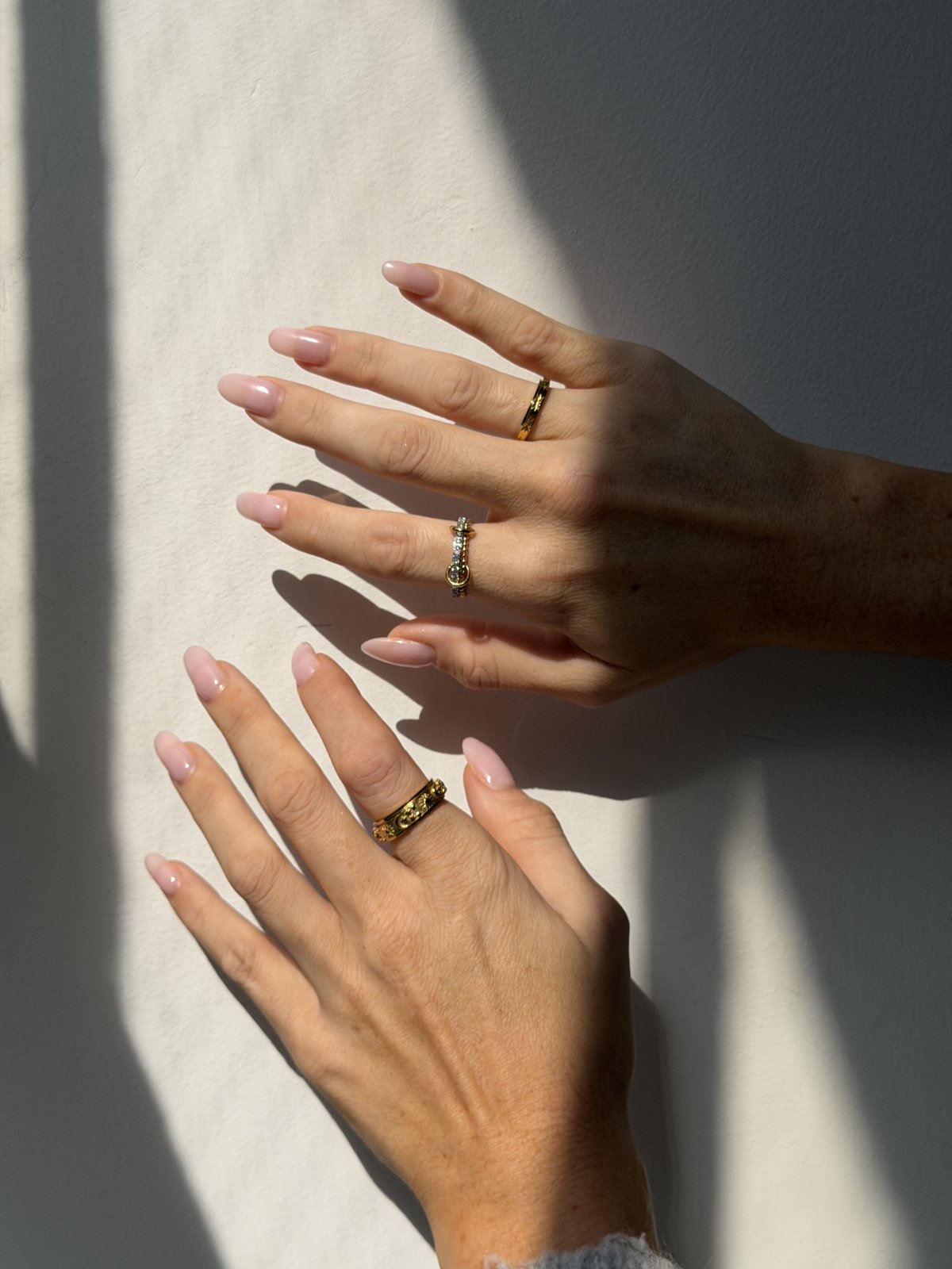 Two hands against a sunlit wall wearing gold Day and Night rings
