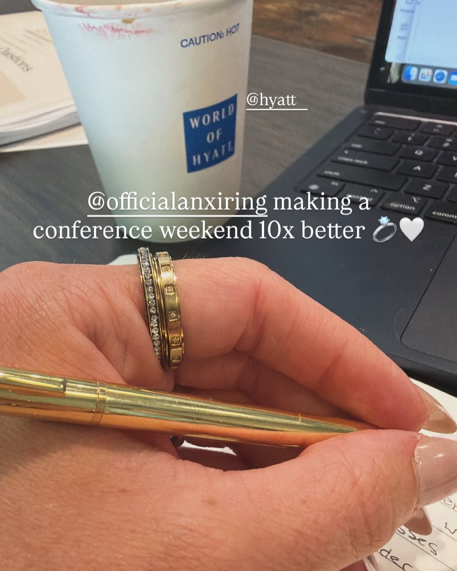 Anxi Ring at a conference, hand with gold rings holding a pen by a laptop