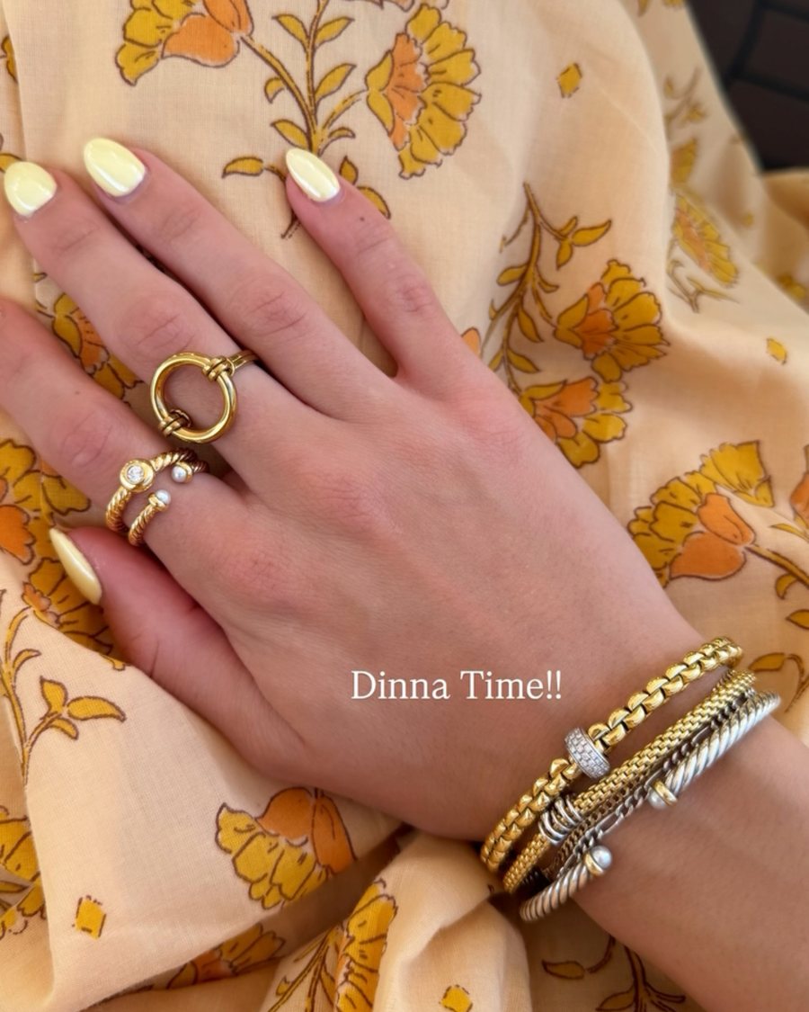 Hand with gold Anxi Rings and bracelets on a yellow floral dress