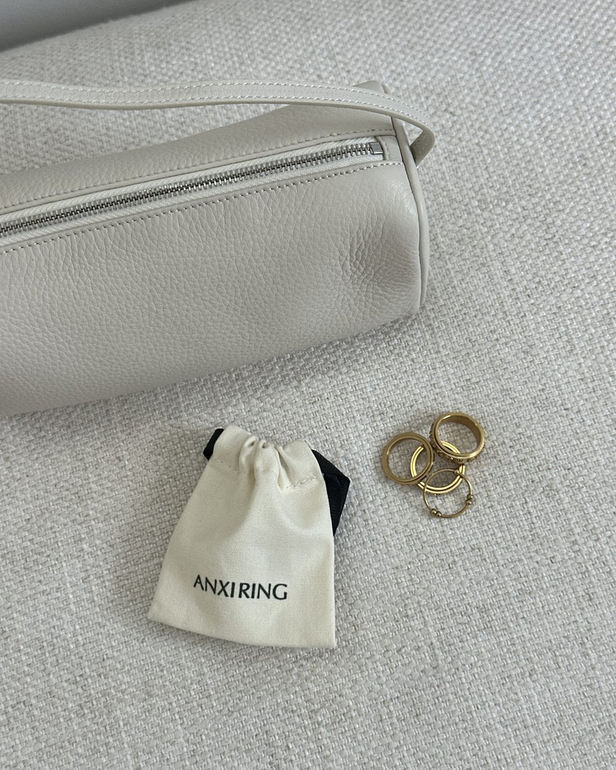 Anxi Ring drawstring pouch and gold rings beside a cream shoulder bag