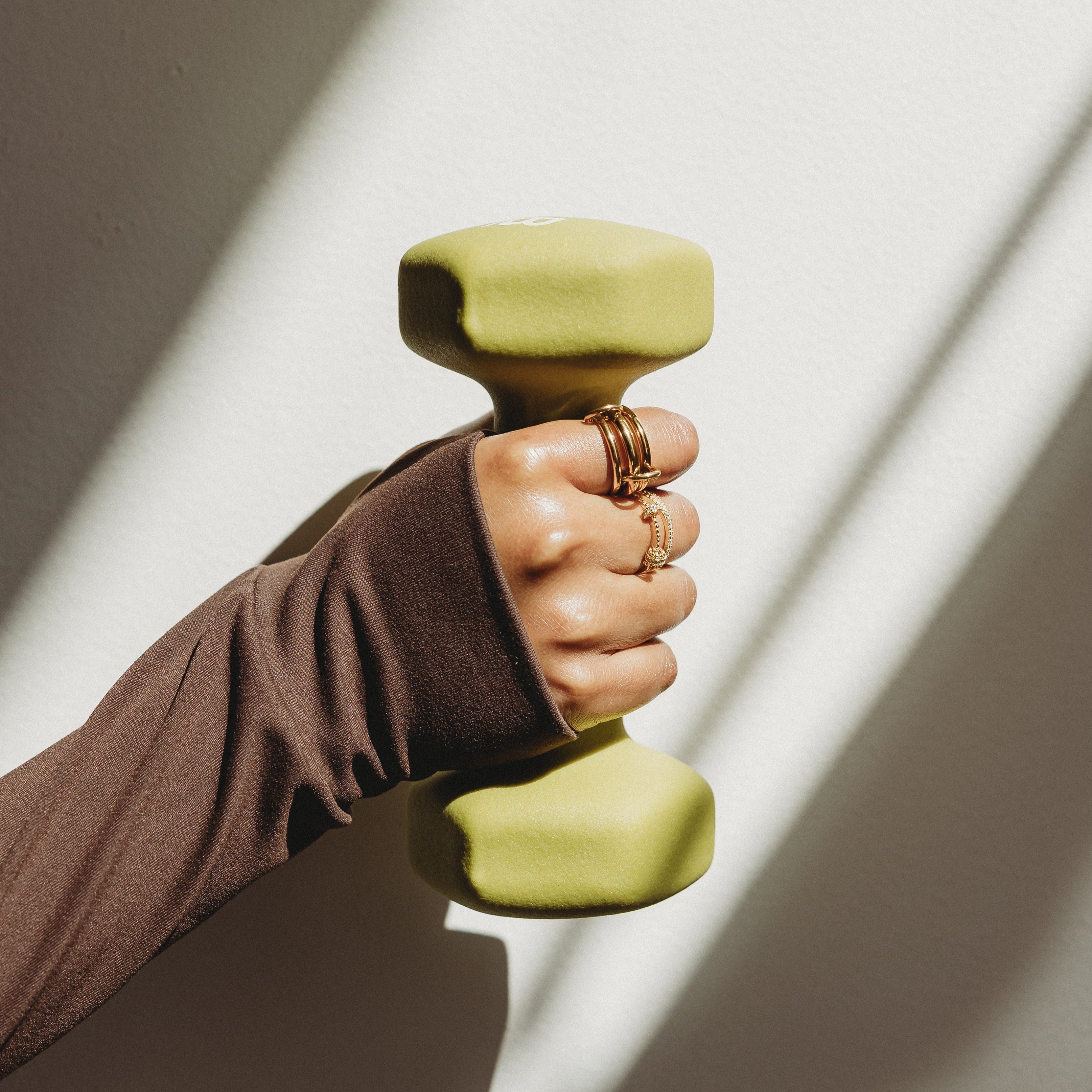 Hand holding a green dumbbell against a neutral background