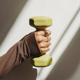 Hand holding a green dumbbell against a neutral background