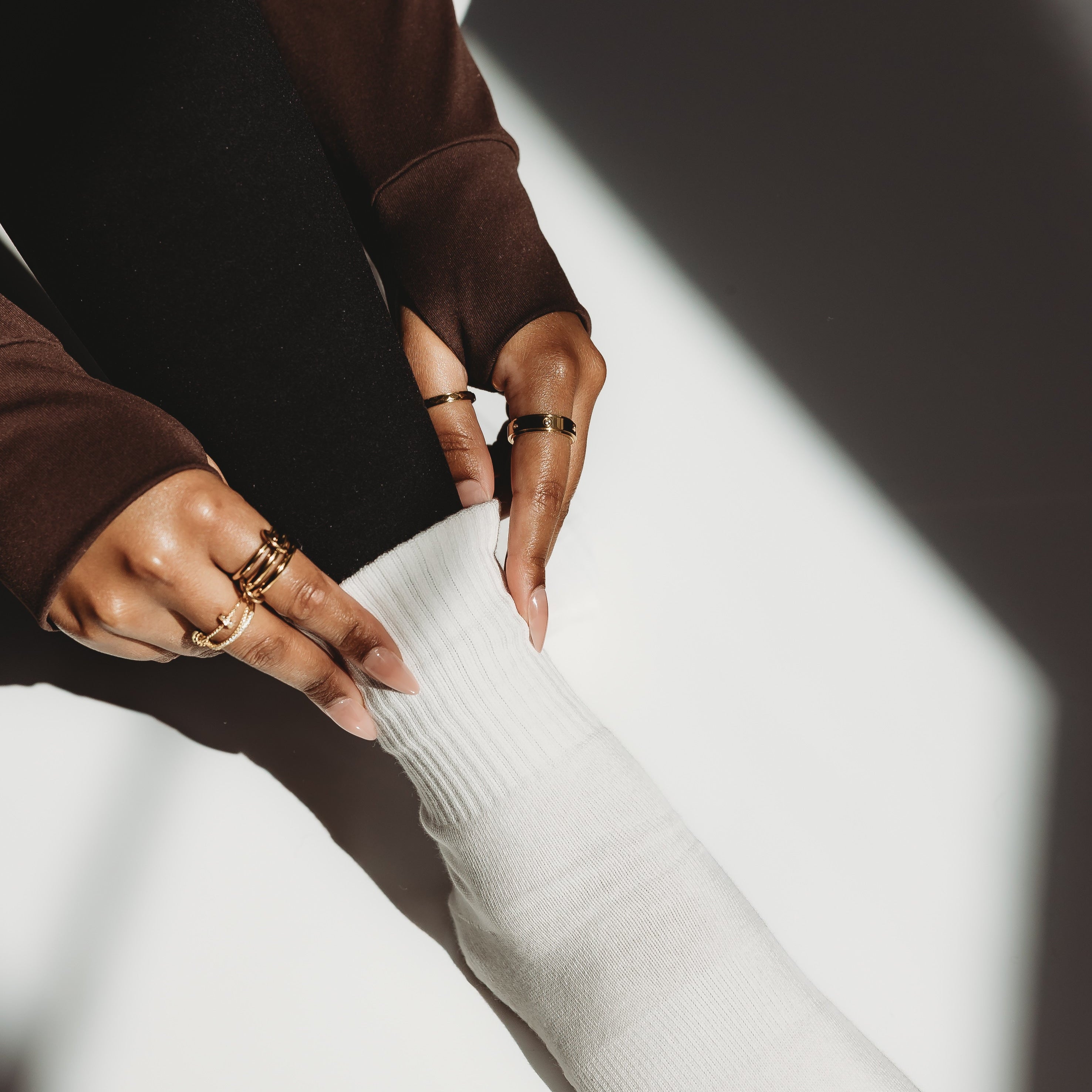 Person wearing a brown sweater and white pants with visible rings on a white background