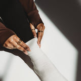 Person wearing a brown sweater and white pants with visible rings on a white background