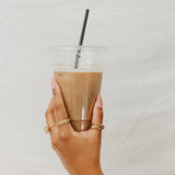 Hand holding a clear plastic cup with a iced coffee beverage and a straw against a plain background