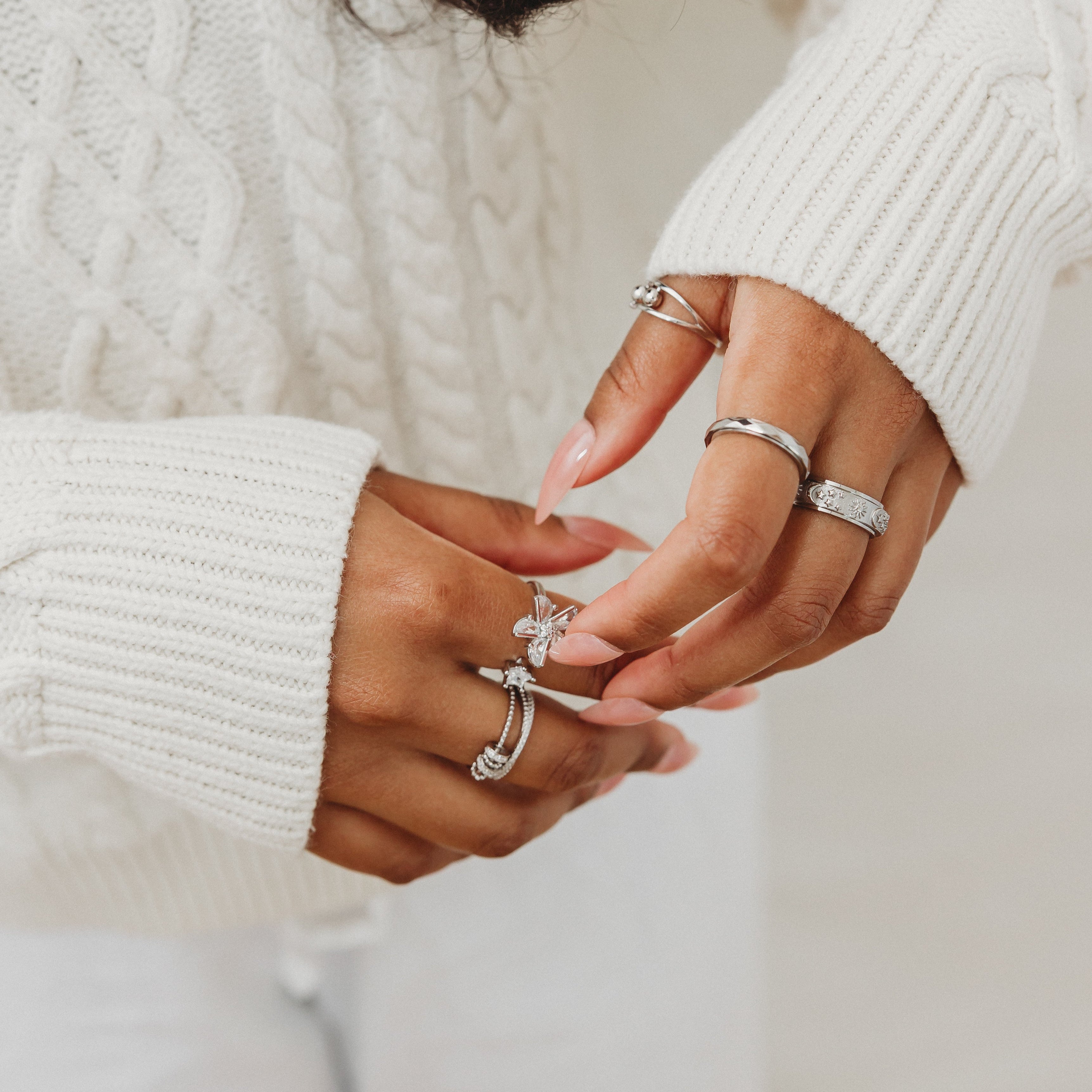 Close-up of hands wearing multiple rings with a blurred white background
