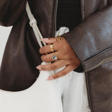Person wearing a brown leather jacket with a focus on jewelry and clothing details.