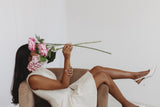 Woman sitting on a chair holding pink flowers against a white background
