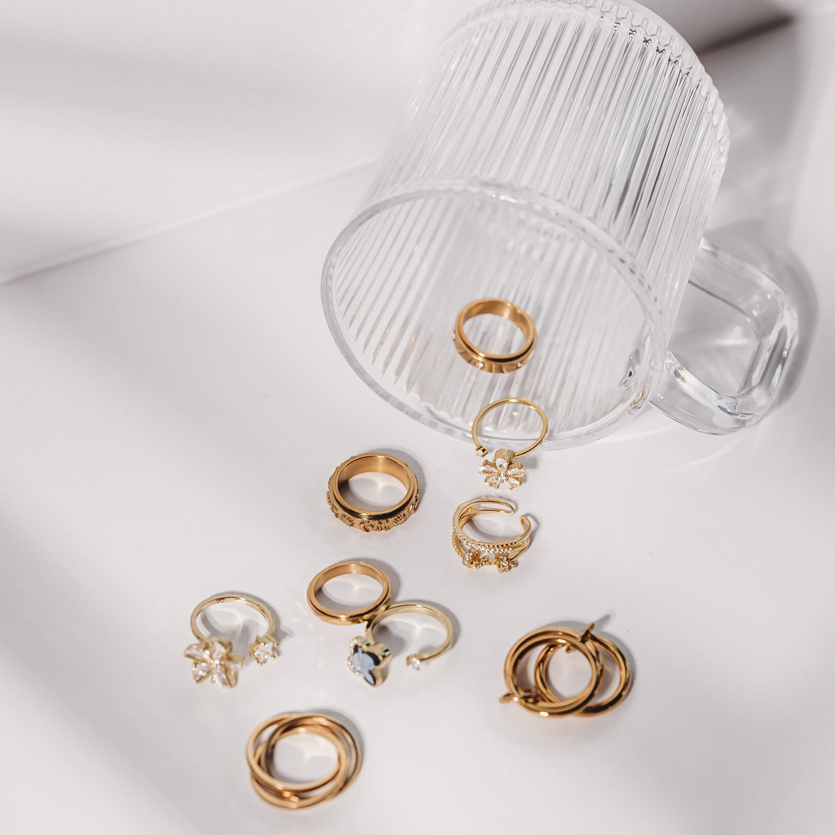 Collection of gold rings on a white surface with a clear glass container.
