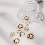 Collection of gold rings on a white surface with a clear glass container.