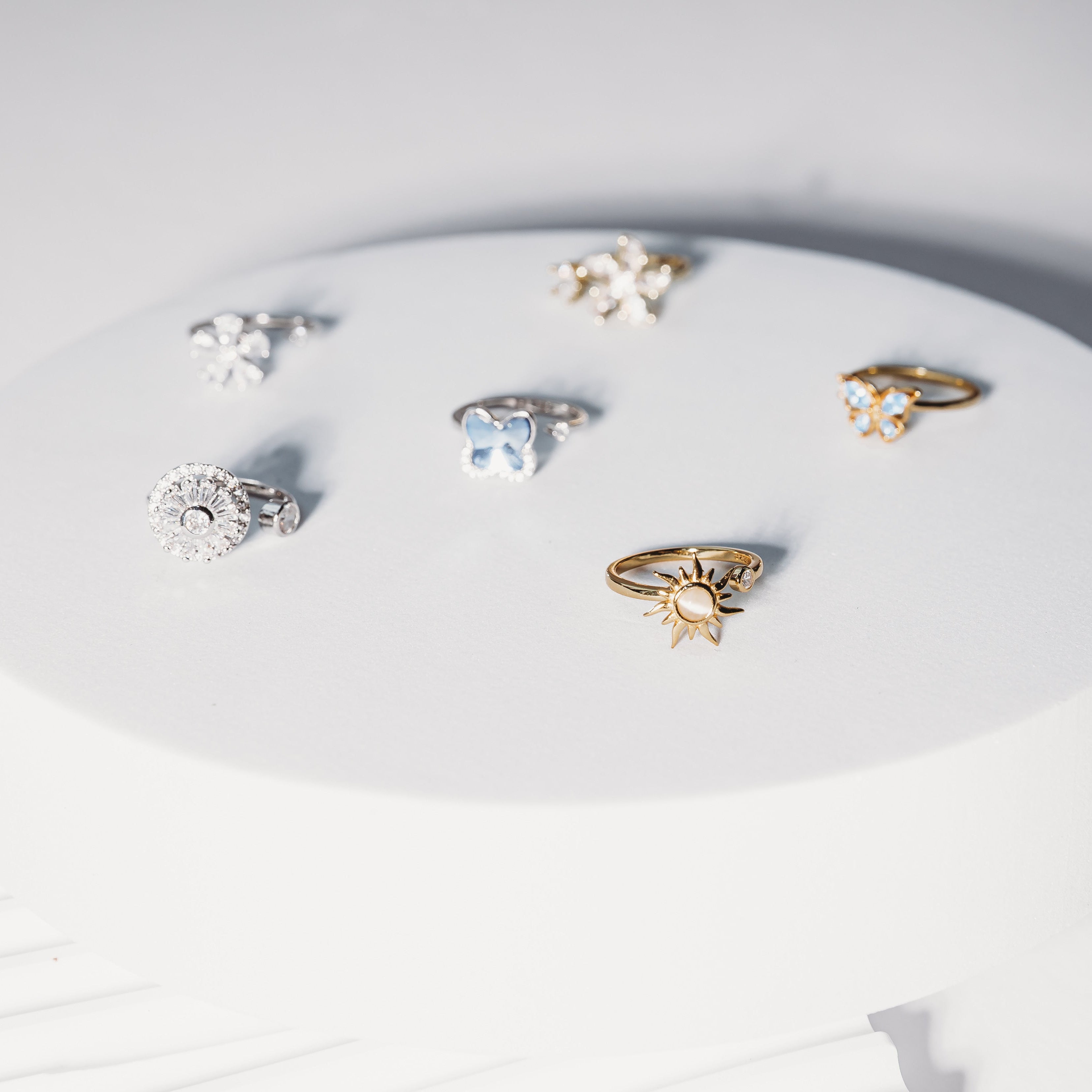 Collection of rings on a white circular stand with a light gray background