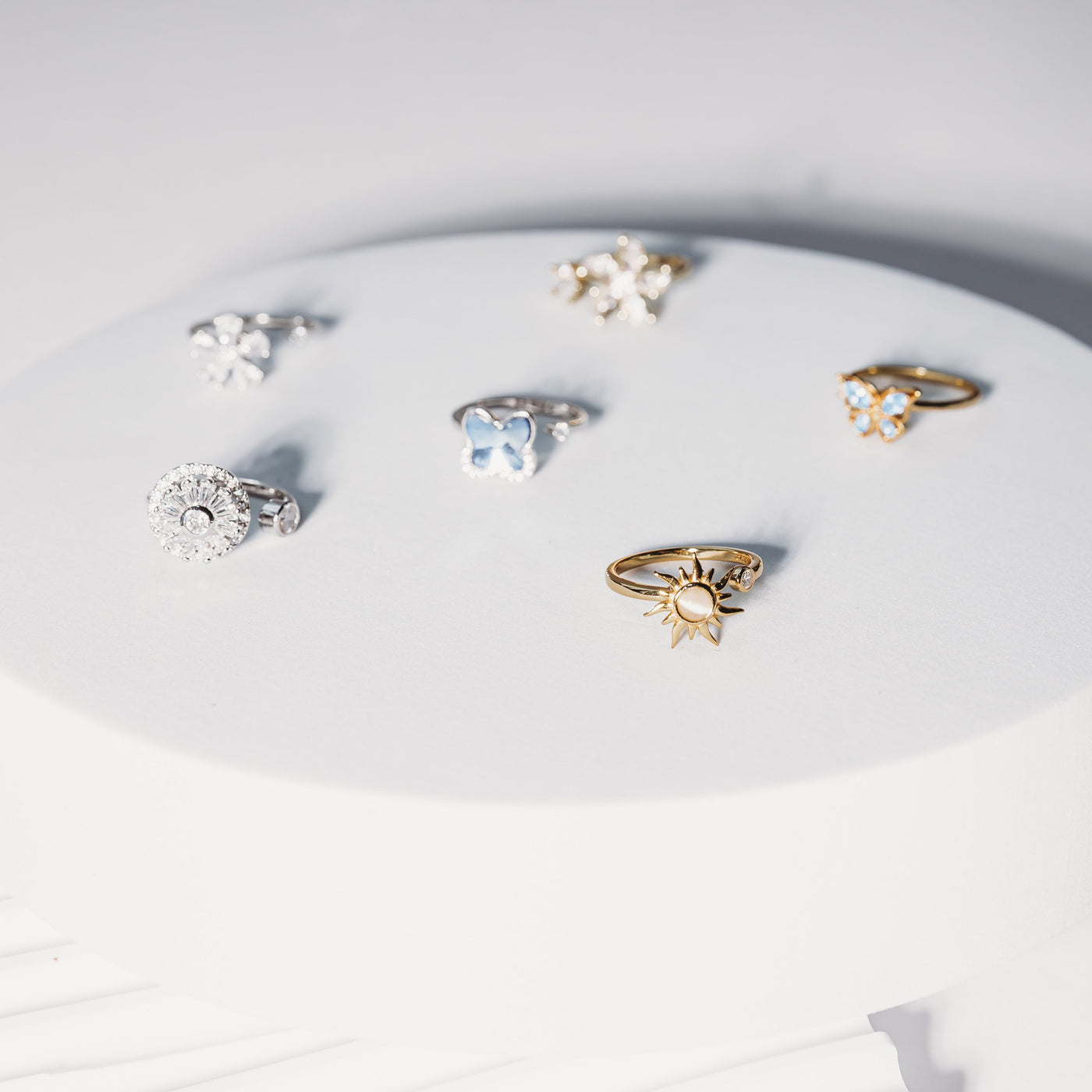 Collection of rings on a white circular stand with a light gray background