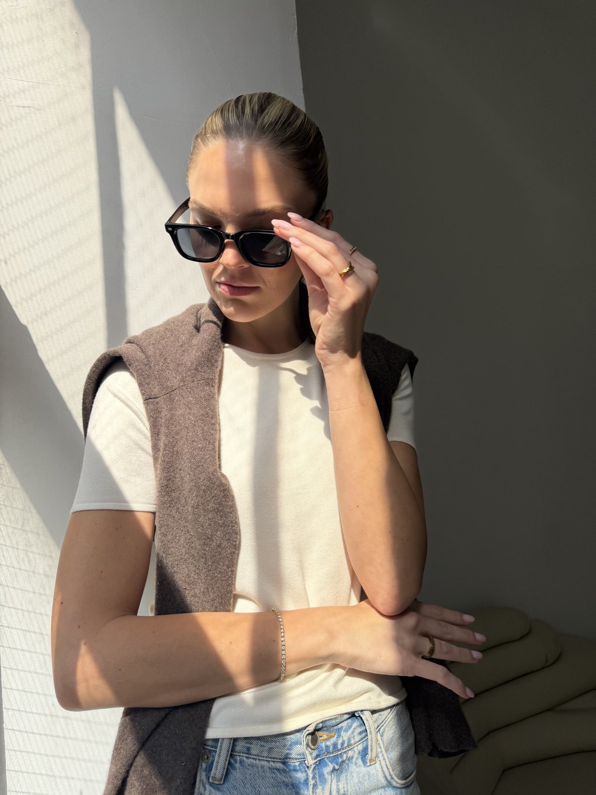 Woman in sunglasses and a knit vest, gold Anxi Ring on her hand in sunlight