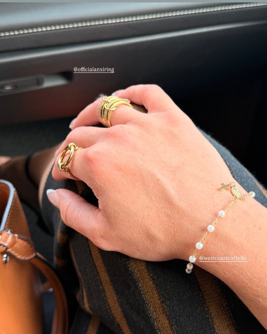 Hand with gold Anxi Rings and a pearl bracelet in the car