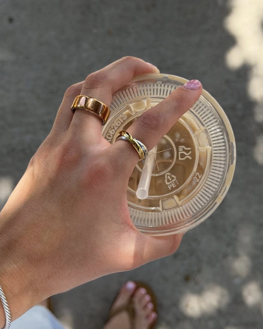 Hand with gold Anxi Rings holding an iced coffee in the sun
