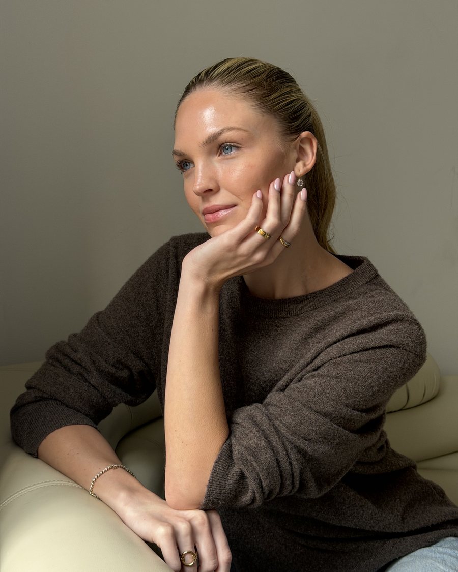 Woman in a brown knit, hand on her cheek with a gold Anxi Ring