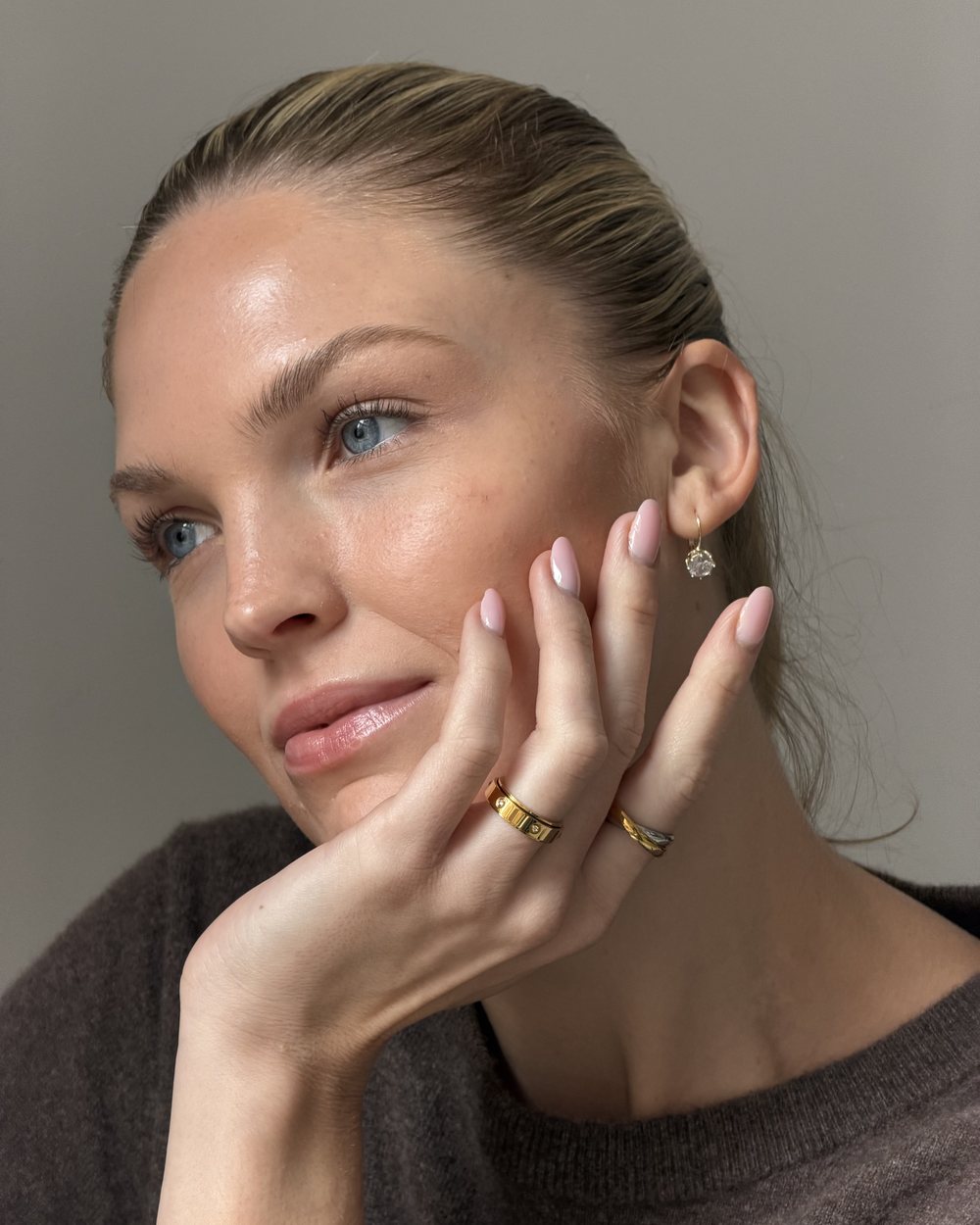 Woman in a brown knit resting her cheek on her hand, gold Anxi Ring