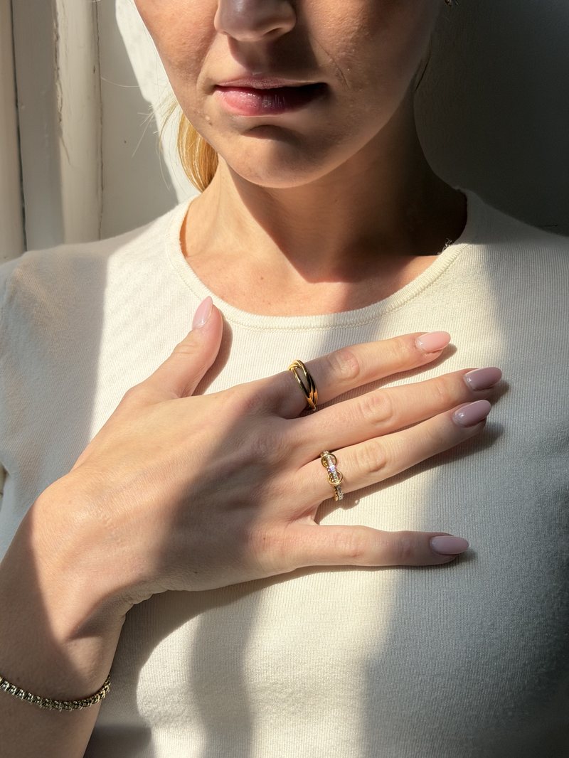 Hand resting on a cream tee, gold Anxi Rings catching the sun