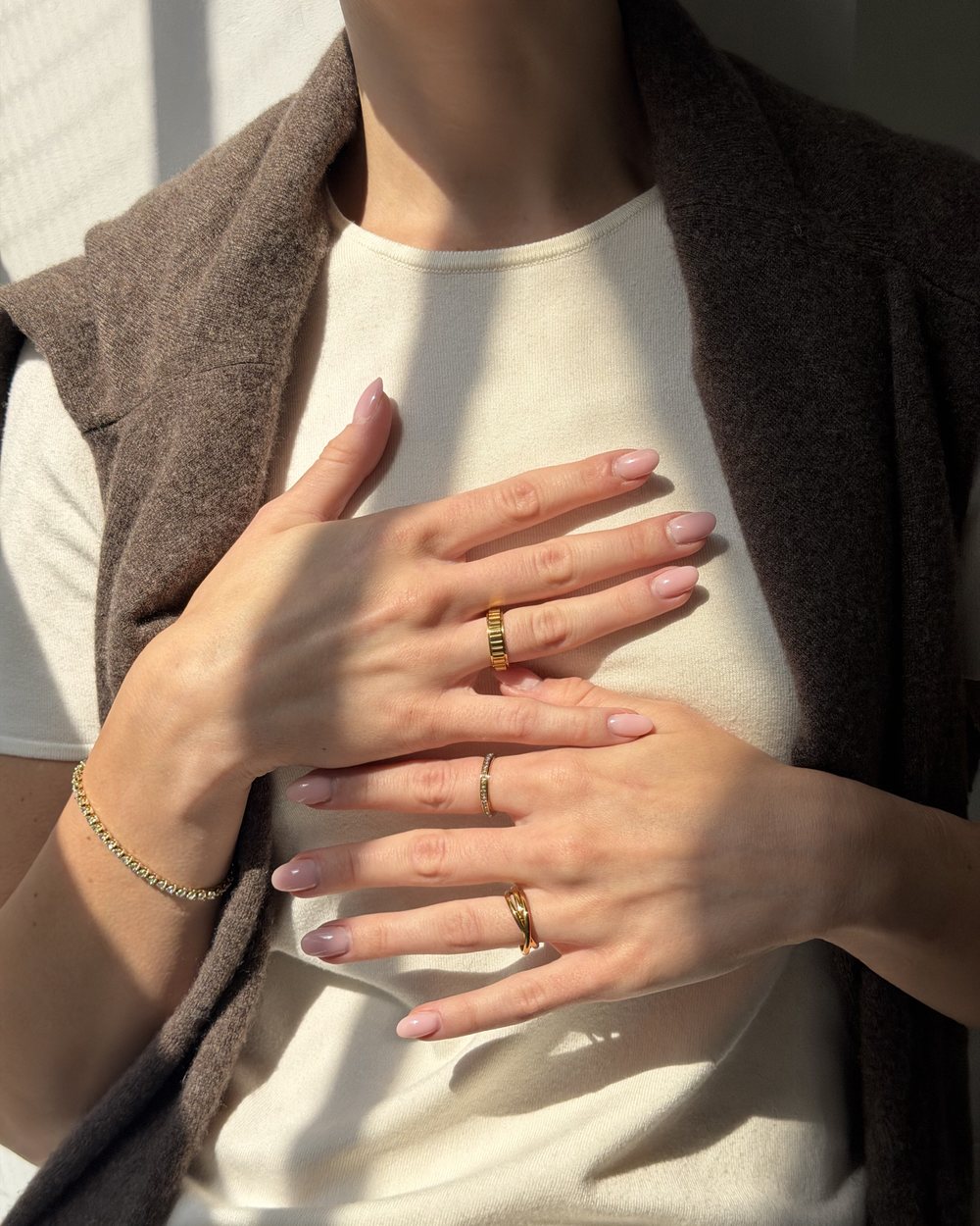 Hands crossed over a cream tee with a knit on the shoulders, gold Anxi Rings on both hands