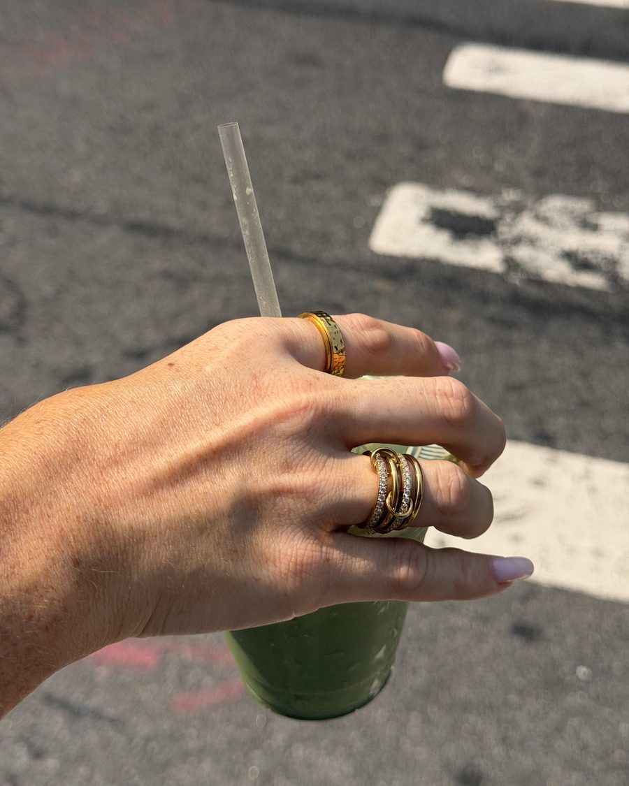 Hand with a gold Anxi Ring stack holding a matcha on a city street