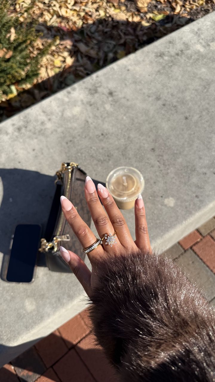 Hand with gold Anxi Rings and a fur sleeve holding a coffee on a stone ledge
