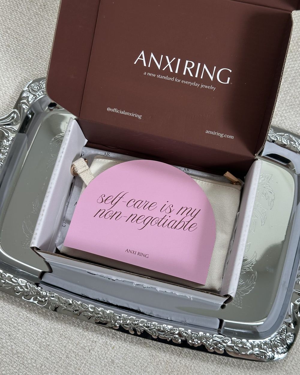 An open Anxi Ring box on a silver tray with a pink self-care is my non-negotiable card