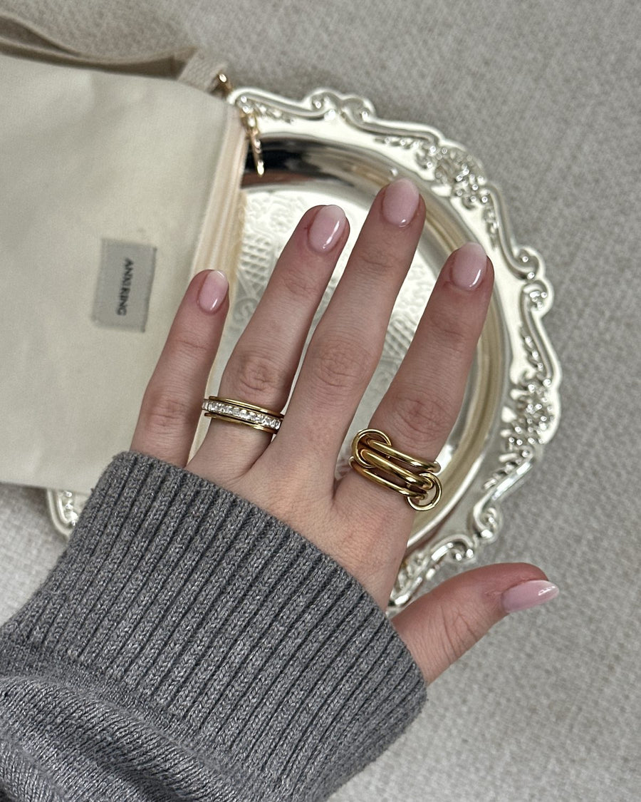 Hand in a grey knit sleeve wearing a gold interlocking Anxi Ring and a pavé band over a silver tray and Anxi Ring pouch