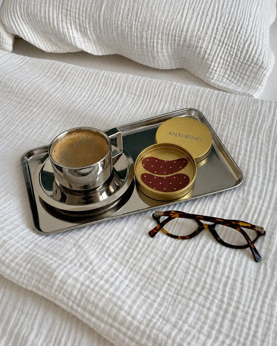 Disturb Me Not eye patch tin on a breakfast tray with a coffee and glasses