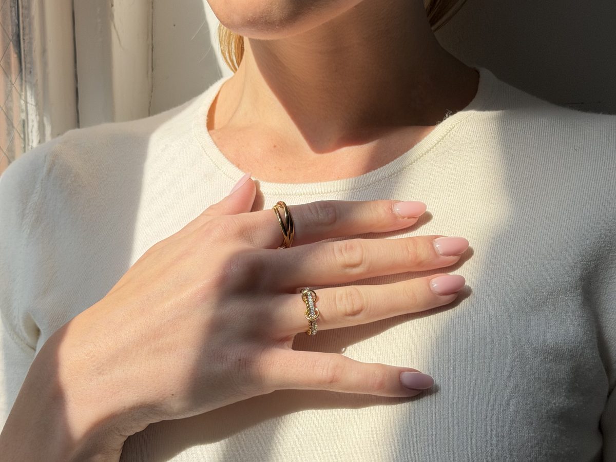Hand resting on her chest in window light, wearing two gold Anxi Rings