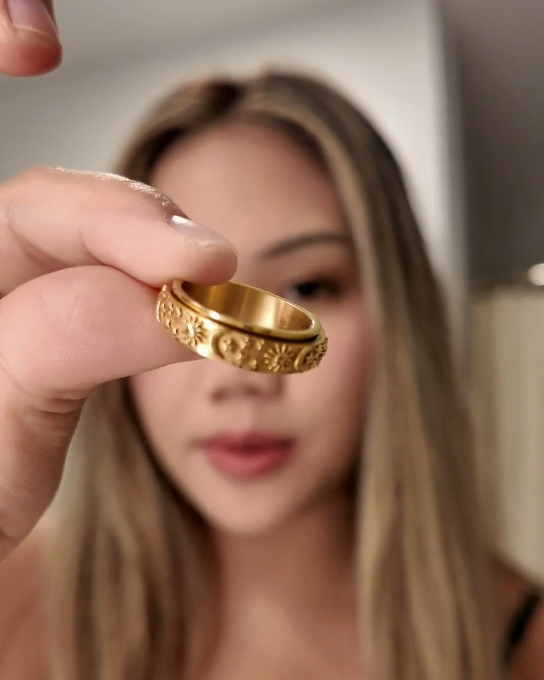 Woman holding a gold Day and Night Anxi Ring up to the camera